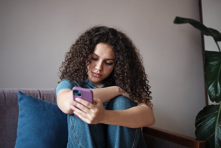 A girl sitting on the couch head down scrolling on her phone with a purple cover.jpg
