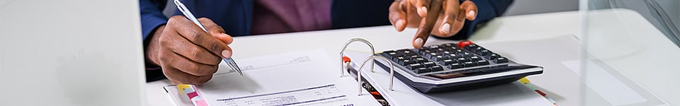 Person at a desk, holding a pen and pressing a calculator