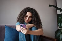Article Image - A girl sitting on the couch head down scrolling on her phone with a purple cover.jpg